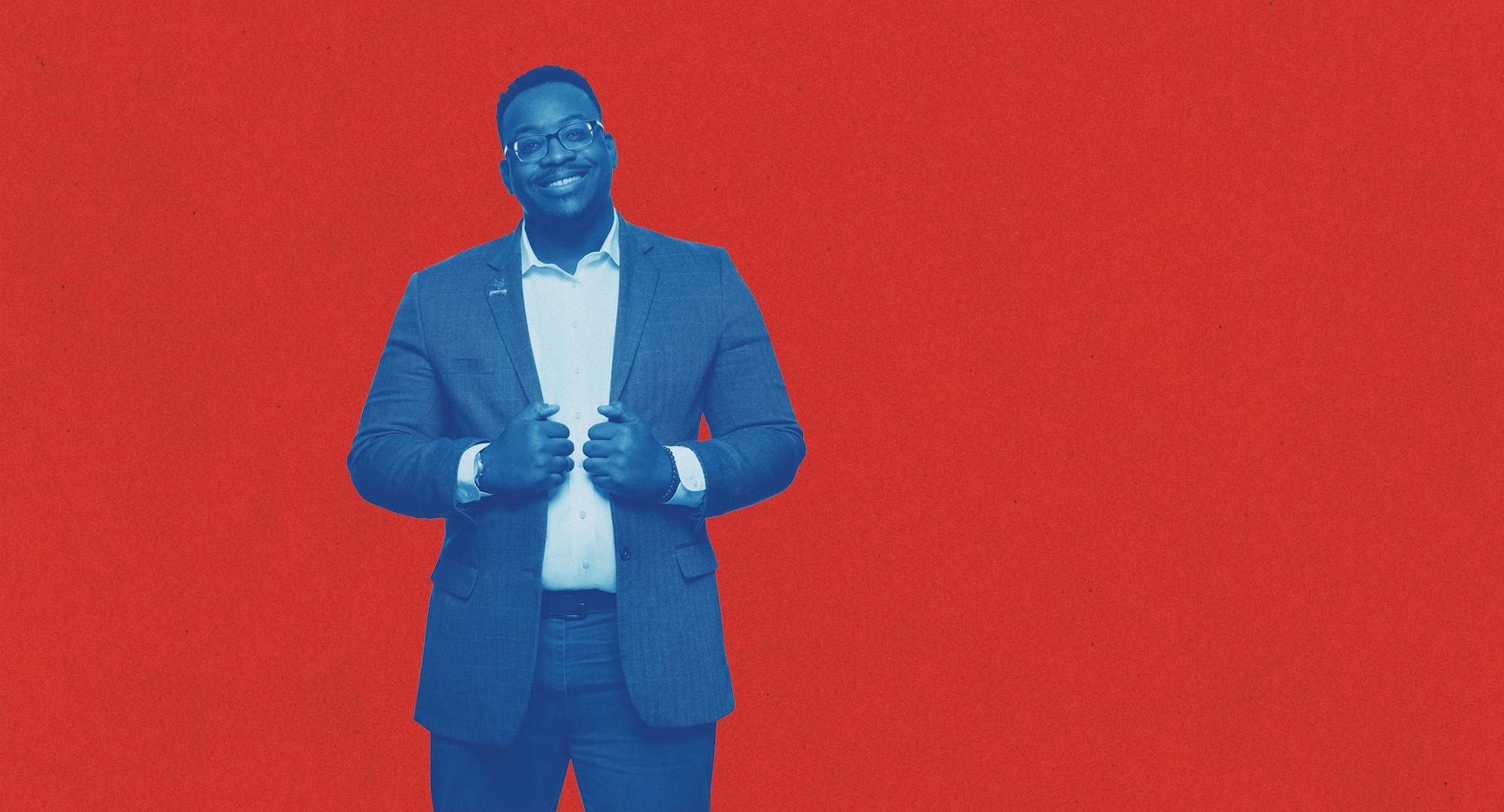 博彩平台推荐 Student dressed in a suit posing and smiling in front of a red background.